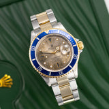 Two-tone Rolex watch with blue bezel on a green background