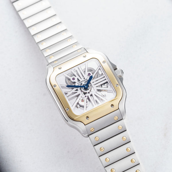 Front view of a Cartier Santos Skeleton WHSA0019 watch featuring a stainless steel and yellow gold case, 39mm size, showcasing an intricate skeleton dial and bold Roman numeral hour markers.